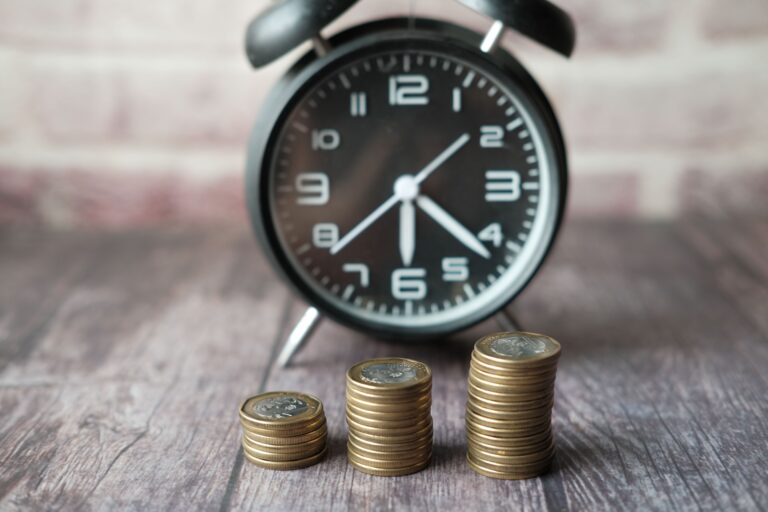 Monedas apiladas junto a un reloj de arena representando el ahorro para el retiro