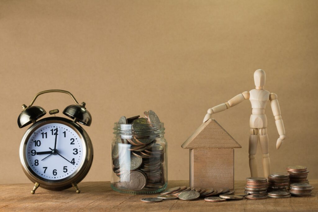 Figura de madera con casa, monedas y reloj simbolizando planificacion financiera