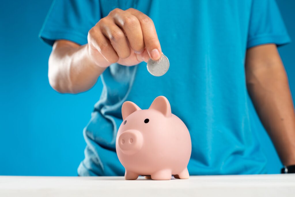 Mano de adulto depositando una moneda en una alcancia representando el ahorro
