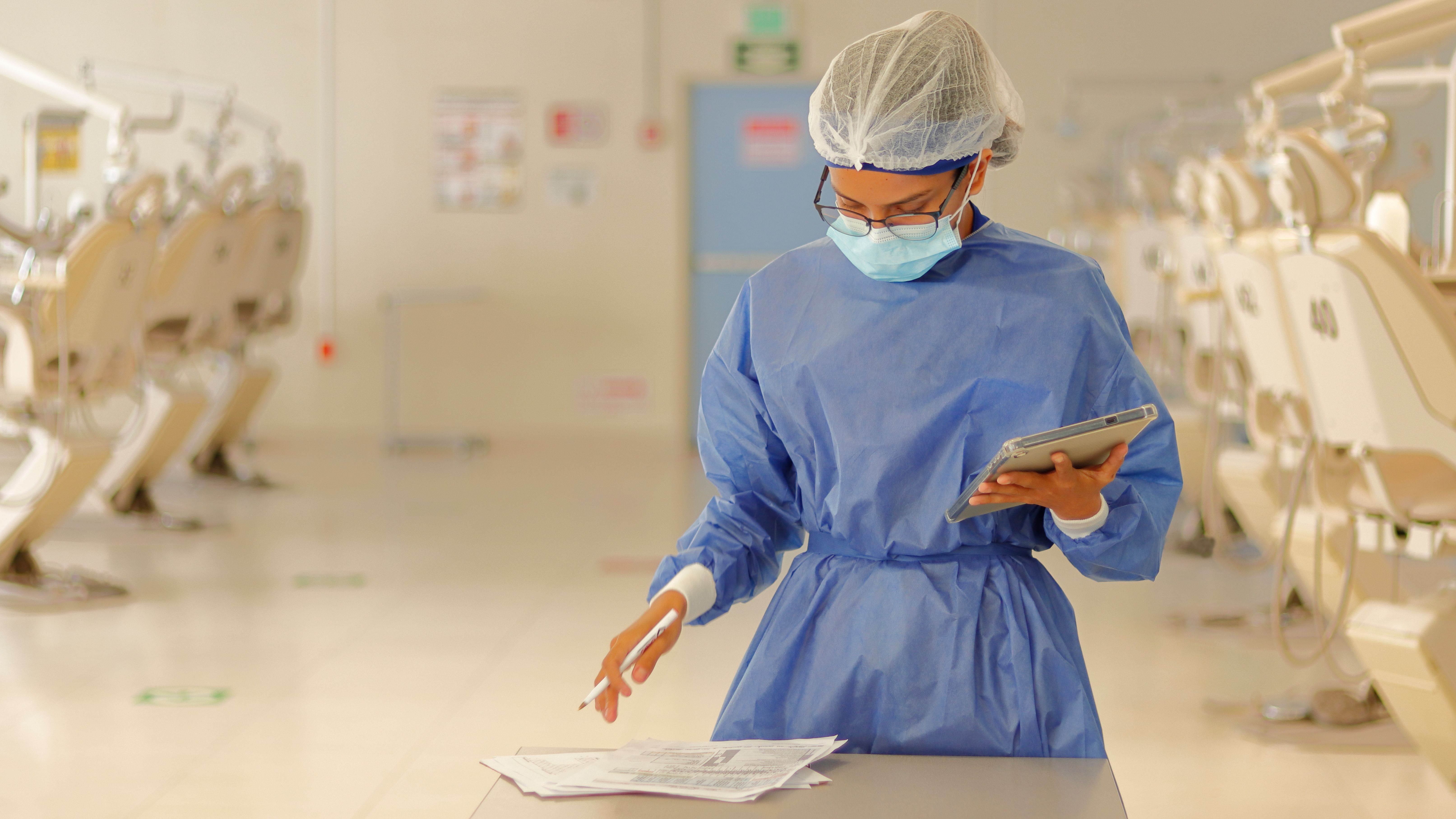 Profesional de salud con equipo de proteccion azul revisando documentos en clinica