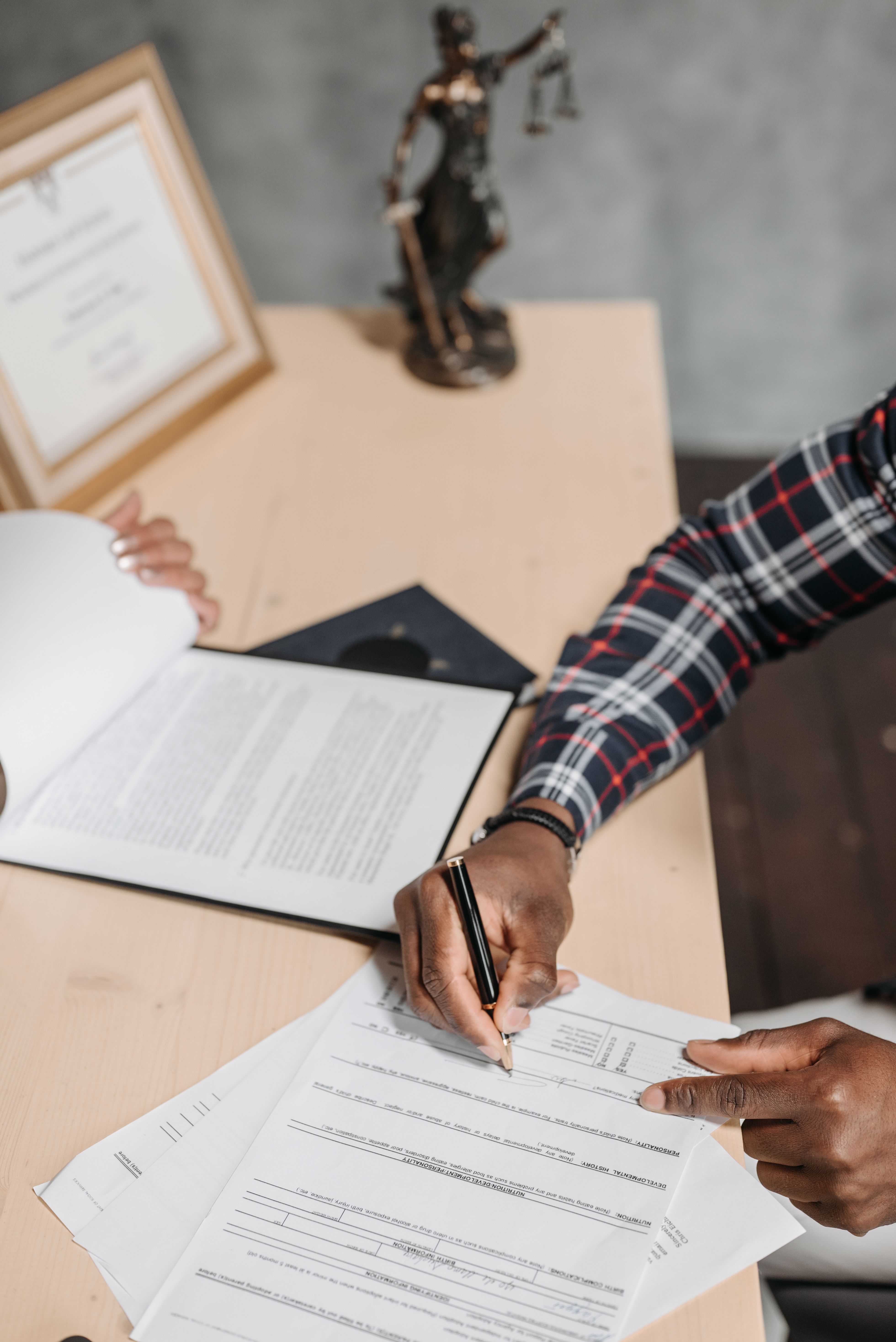 Manos de una persona firmando documentos oficiales en un escritorio de oficina — Foto de Pavel Danilyuk en Pexels (https://www.pexels.com/photo/man-signing-documents-on-desk-8152746/)