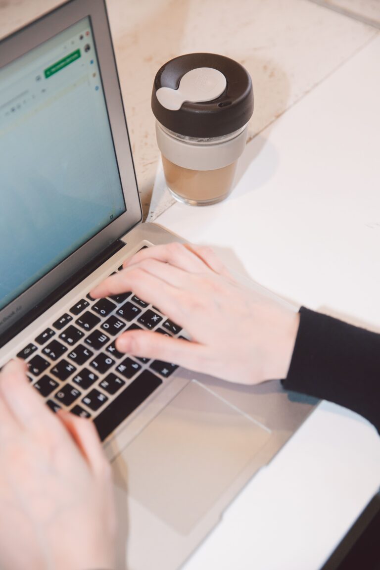 Manos escribiendo en una laptop con una taza de cafe cerca, trabajo remoto y tecnologia