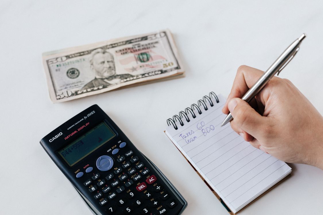 Persona calculando gastos con calculadora, dinero en efectivo y cuaderno de notas sobre escritorio